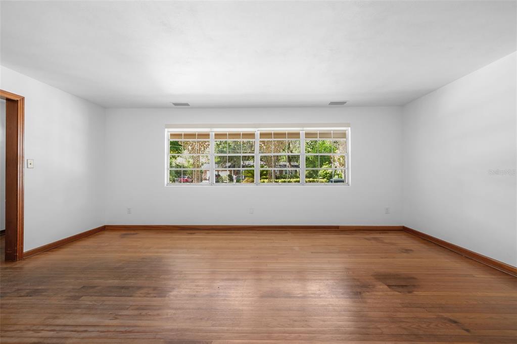 An empty room with white walls, hardwood floors, and a large window overlooking trees — 3716 SW 6TH PLACE, GAINESVILLE, FL