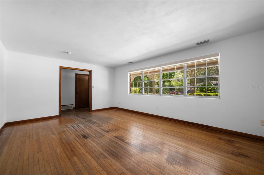 An empty room features hardwood floors, white walls, and a large window with blinds — 3716 SW 6TH PLACE, GAINESVILLE, FL