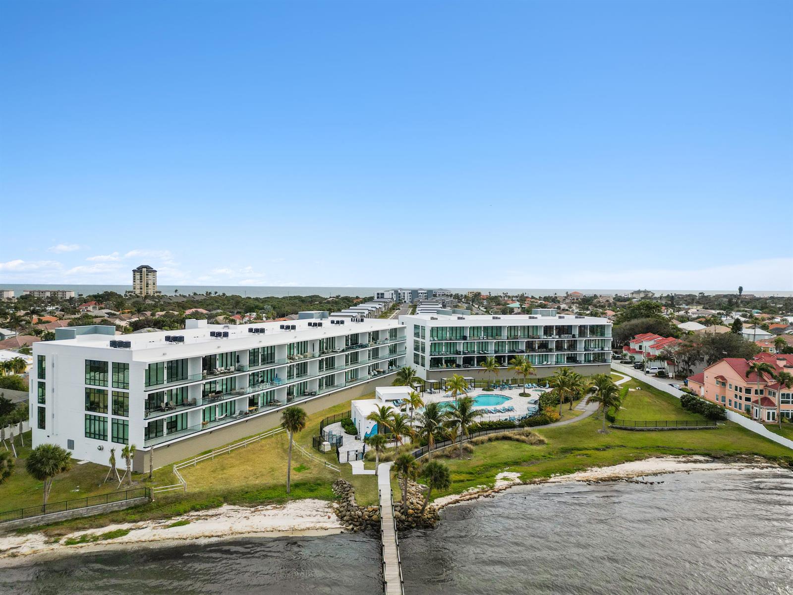 An aerial view shows a modern white apartment complex with a pool near the water — 475 Strand Drive, Melbourne Beach FL 32951, MELBOURNE BEACH, FL