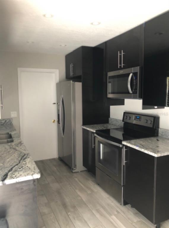 A kitchen features dark cabinets, stainless steel appliances, granite countertops, and light-colored wood-look flooring — 2115 DARDANELLE DRIVE, ORLANDO, FL