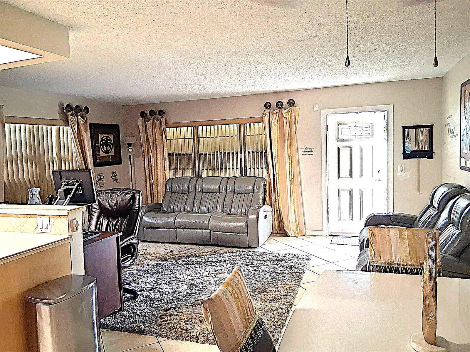 A living room features a grey sofa, a desk, tile flooring, and a front door — 6 Northampton # A, West Palm Beach FL 33417, WEST PALM BEACH, FL