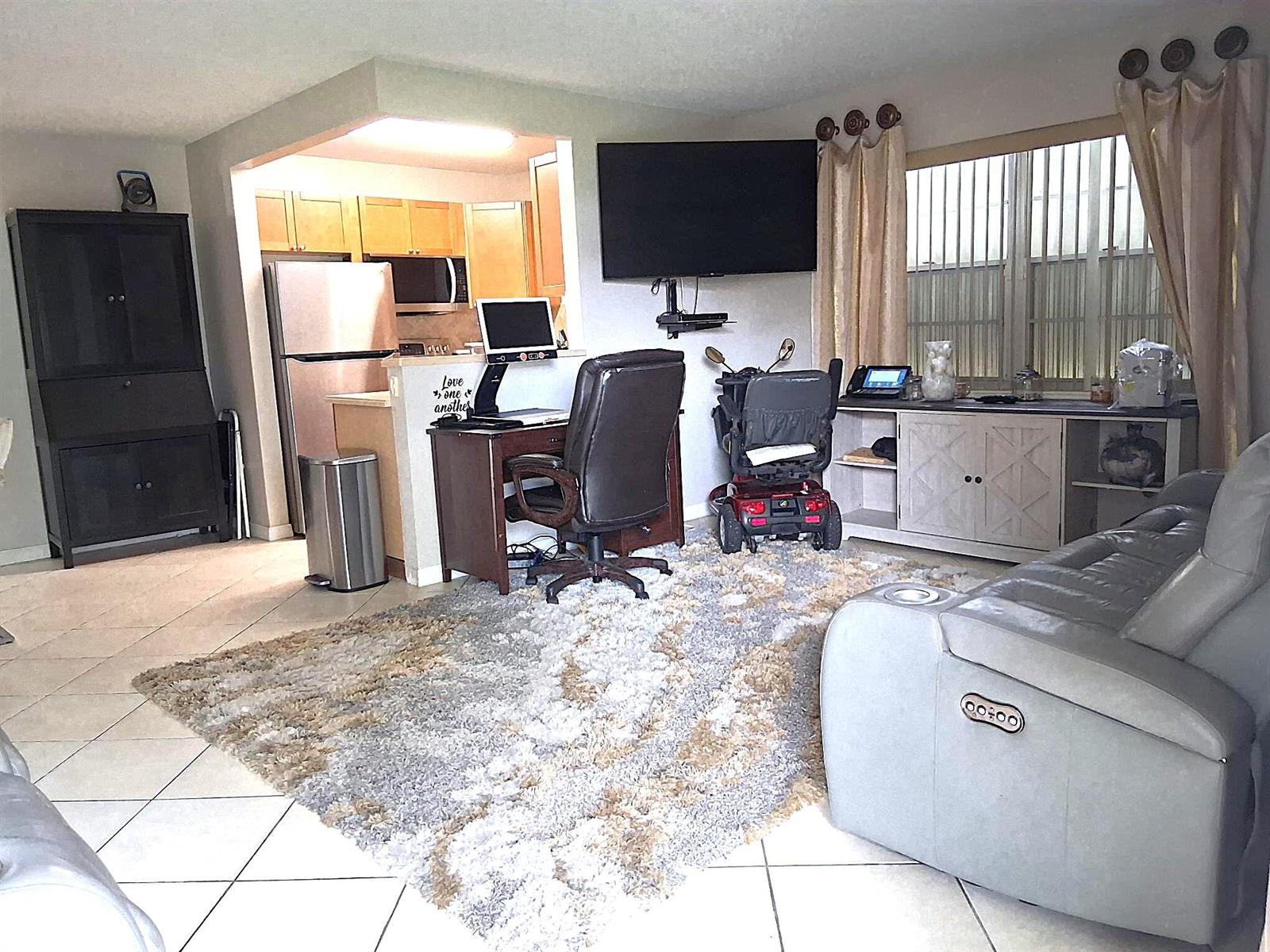 A living room with a desk, a mobility scooter, a wall-mounted television, and a rug — 6 Northampton # A, West Palm Beach FL 33417, WEST PALM BEACH, FL