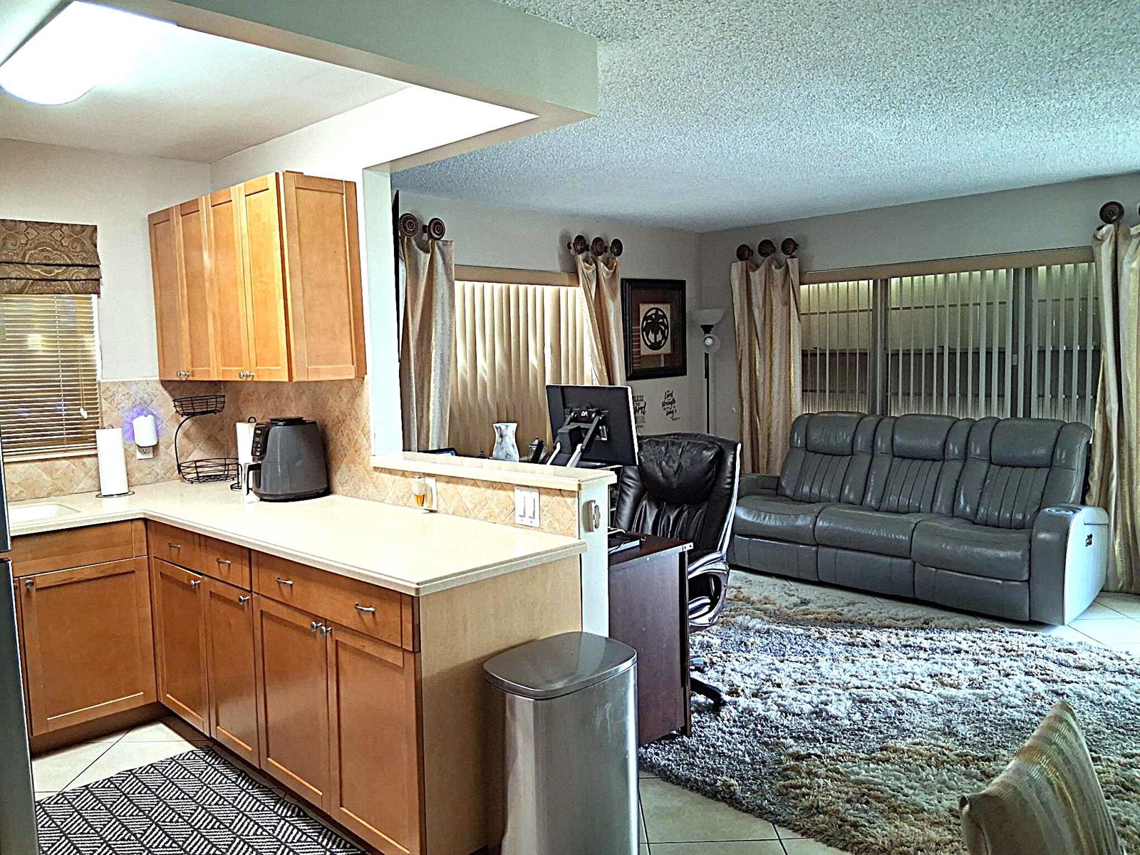 A kitchen with wood cabinets and a breakfast bar overlooks a living room with carpet — 6 Northampton # A, West Palm Beach FL 33417, WEST PALM BEACH, FL