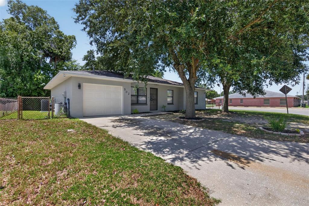A single-story gray house with a one-car garage and a concrete driveway under large trees — 502 LOOMIS TRAIL, DAYTONA BEACH, FL