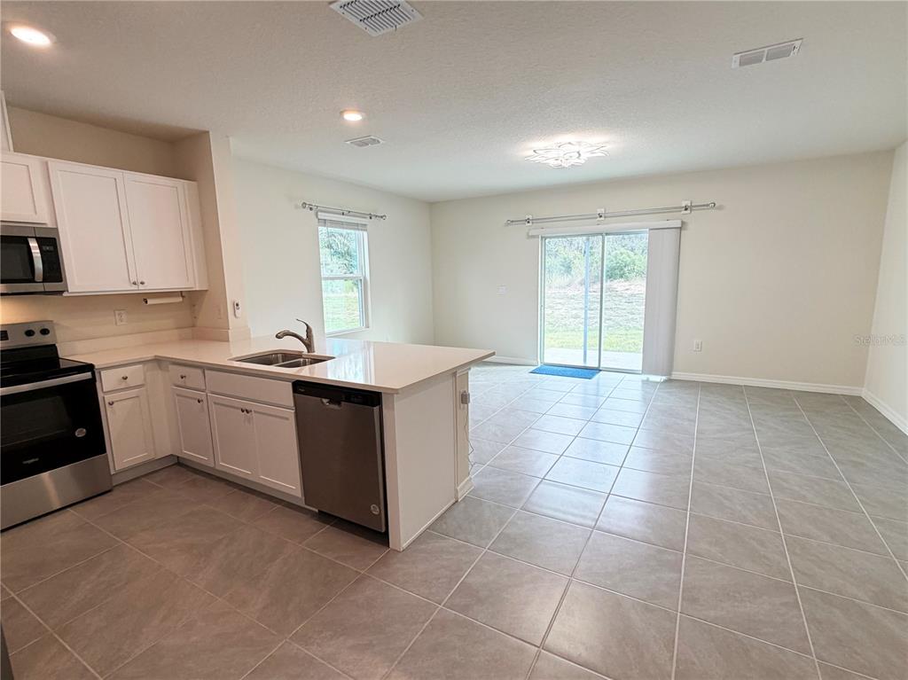 A kitchen with white cabinets and a center island opens to a tiled living area — 3164 GOOSE ROAD, DAVENPORT, FL