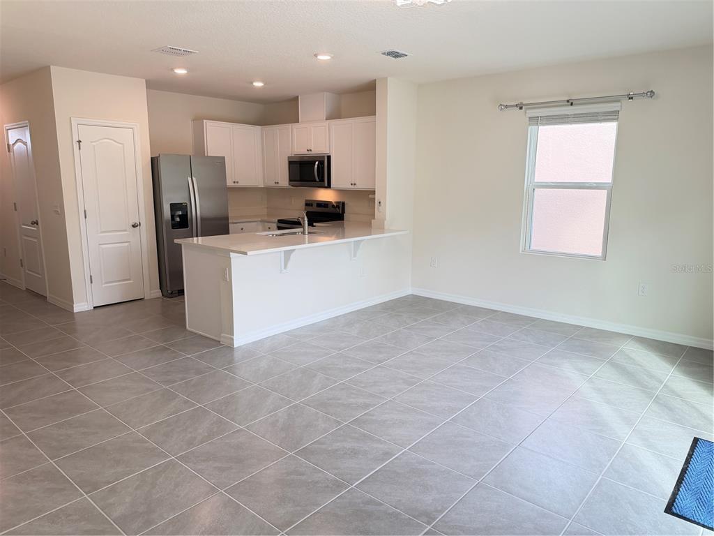 A kitchen with white cabinets, stainless steel appliances, and a breakfast bar overlooks a room — 3164 GOOSE ROAD, DAVENPORT, FL