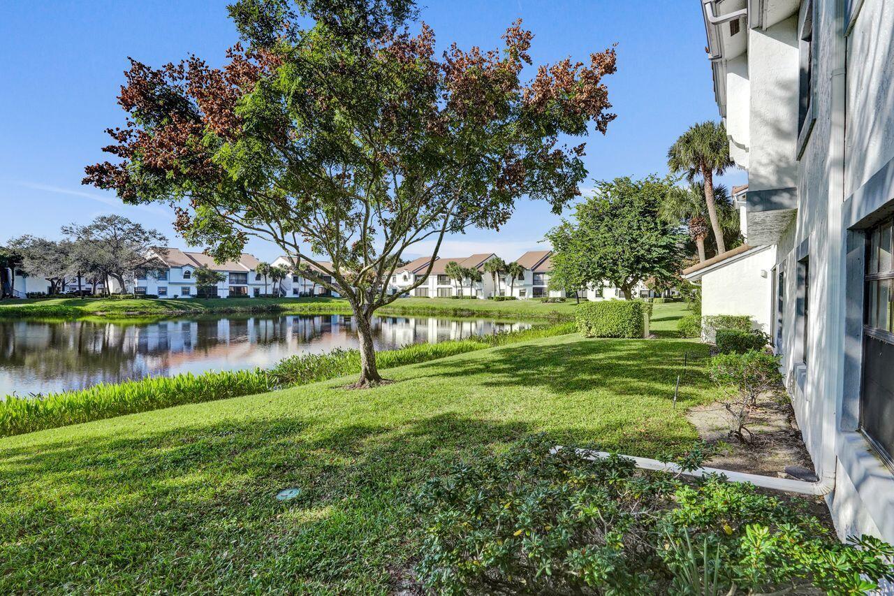 A view of a grassy lawn, a pond, and residential buildings under a clear sky — 5415 Verona Drive # I, Boynton Beach FL 33437, BOYNTON BEACH, FL