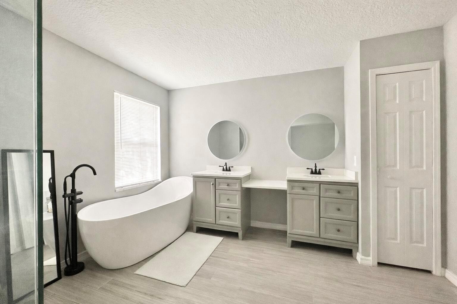 A modern bathroom features a freestanding tub, double vanity with gray cabinets, and circular mirrors — 4410 Pine Gold Avenue, FL 32712, FL