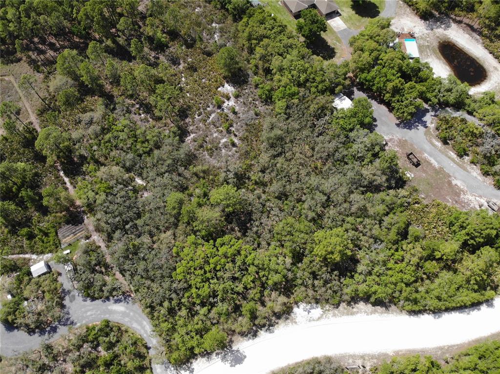 An aerial view shows a wooded, undeveloped lot bordered by paved roads and nearby houses — 1328 R E BYRD ROAD, FROSTPROOF, FL