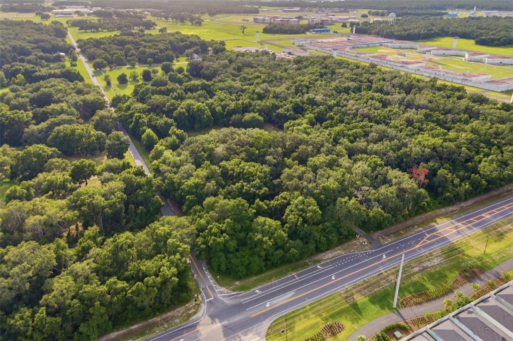 An aerial view shows a wooded lot adjacent to a road and a large facility — 7112 MARSH BEND TRAIL, WILDWOOD, FL