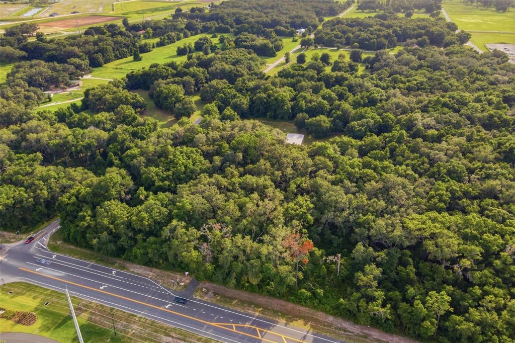 An aerial view shows a large, wooded lot bordering a multi-lane paved road — 7112 MARSH BEND TRAIL, WILDWOOD, FL