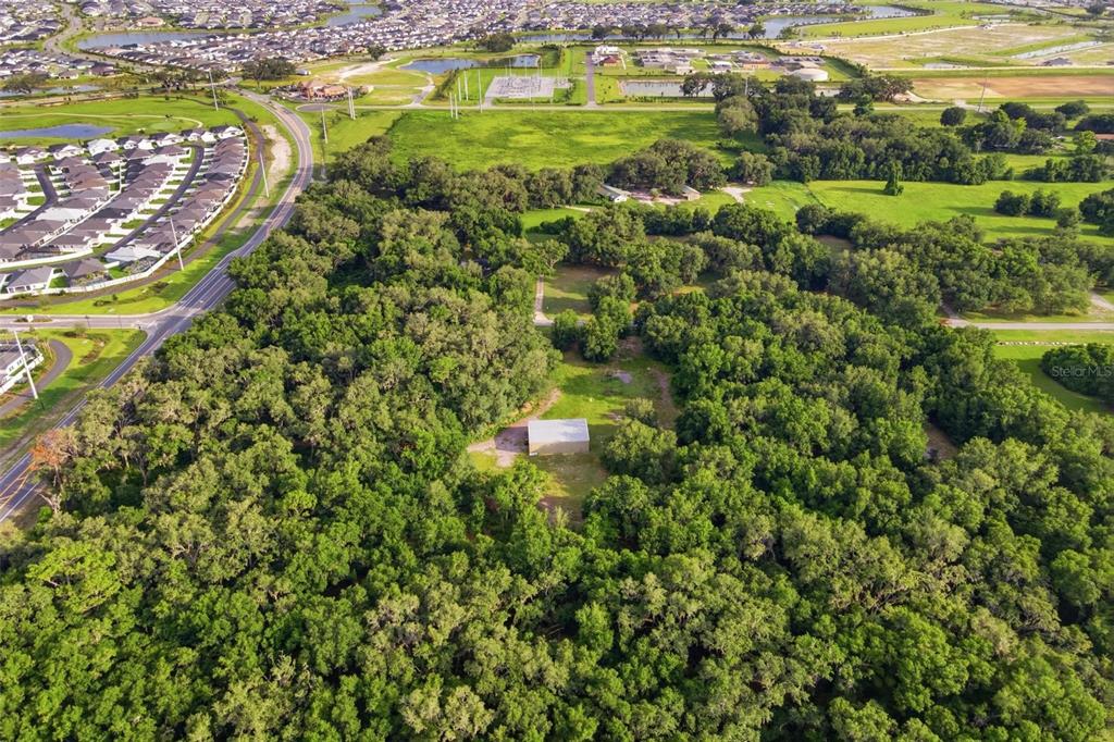 An aerial view shows a small rectangular building surrounded by dense forest and nearby roads — 7112 MARSH BEND TRAIL, WILDWOOD, FL