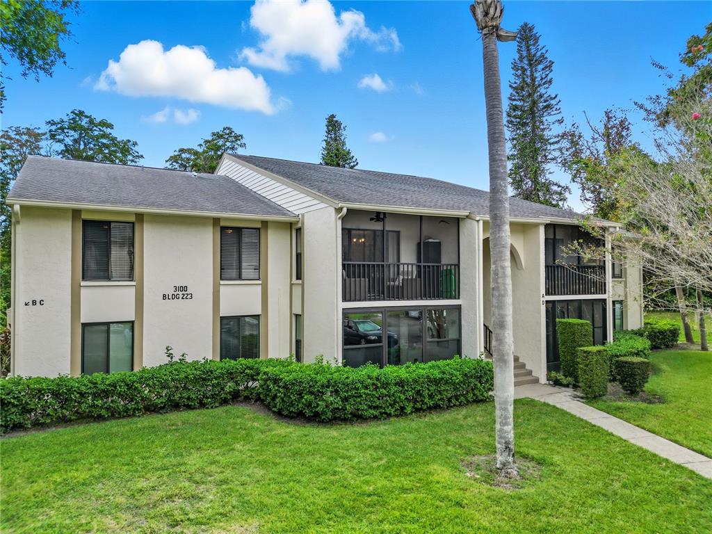A two-story apartment building with beige stucco walls, screened balconies, and a manicured hedge — 3100 LAKE PINE WAY UNIT A2, TARPON SPRINGS, FL