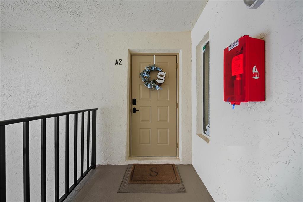 An exterior view of a tan apartment door with a wreath and a fire alarm — 3100 LAKE PINE WAY UNIT A2, TARPON SPRINGS, FL