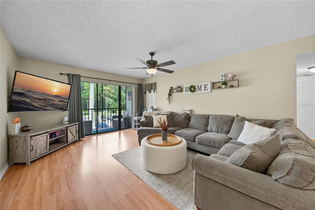 A living room features a grey sectional sofa, a round ottoman, and a wall-mounted television — 3100 LAKE PINE WAY UNIT A2, TARPON SPRINGS, FL