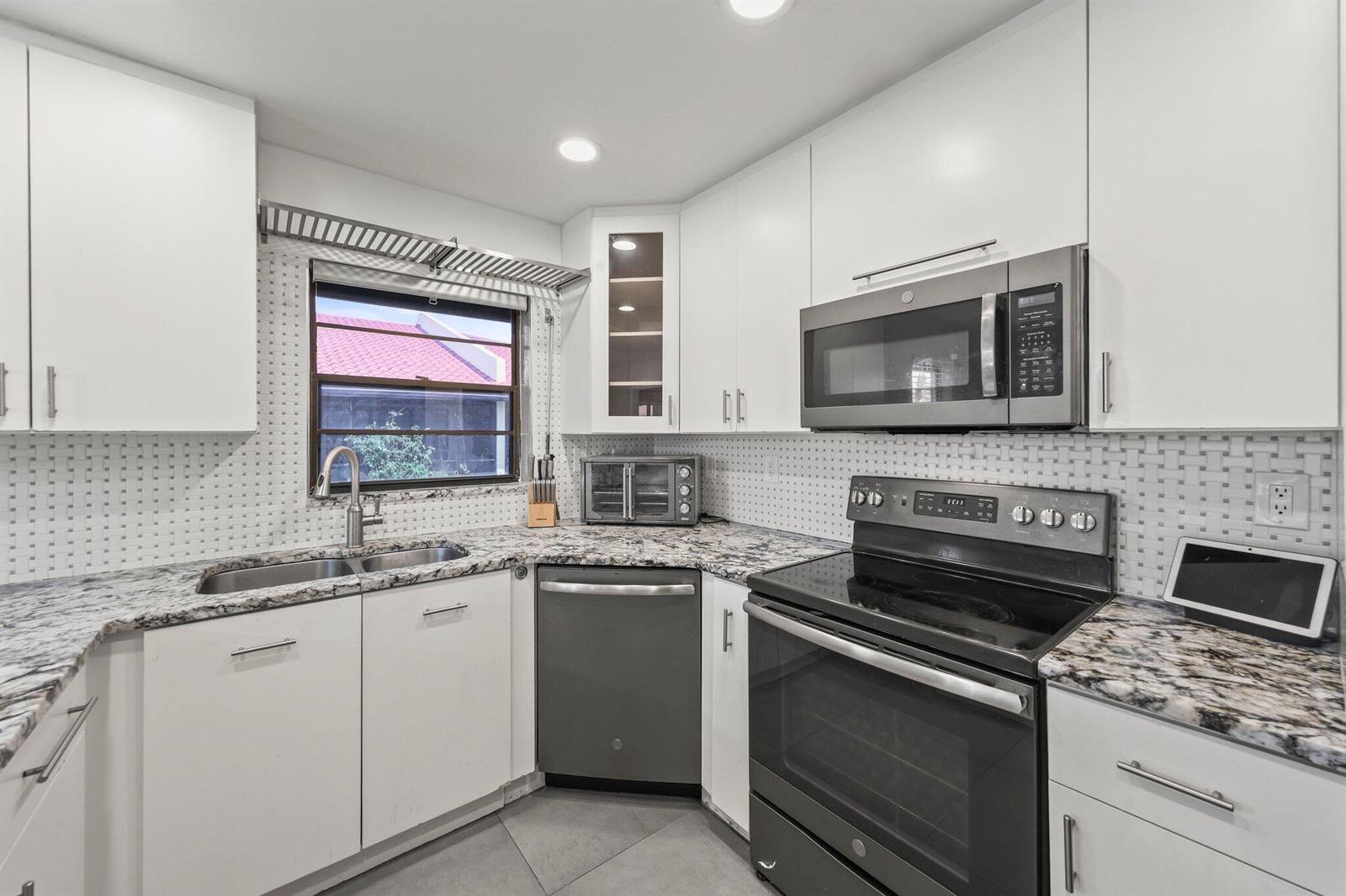 A kitchen with white cabinets, granite countertops, stainless steel appliances, and a tiled backsplash — 41 Bethesda Park Circle # K41, Boynton Beach FL 33435, BOYNTON BEACH, FL