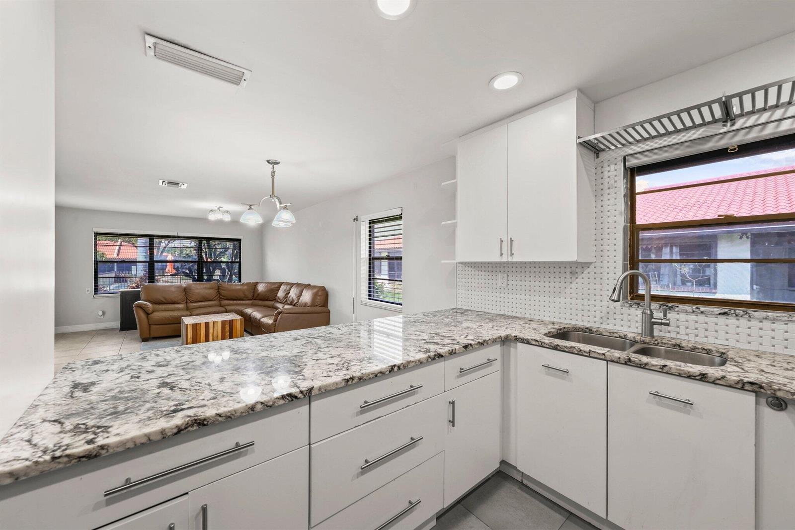 A kitchen with white cabinets and granite countertops overlooks a living room with a sofa — 41 Bethesda Park Circle # K41, Boynton Beach FL 33435, BOYNTON BEACH, FL