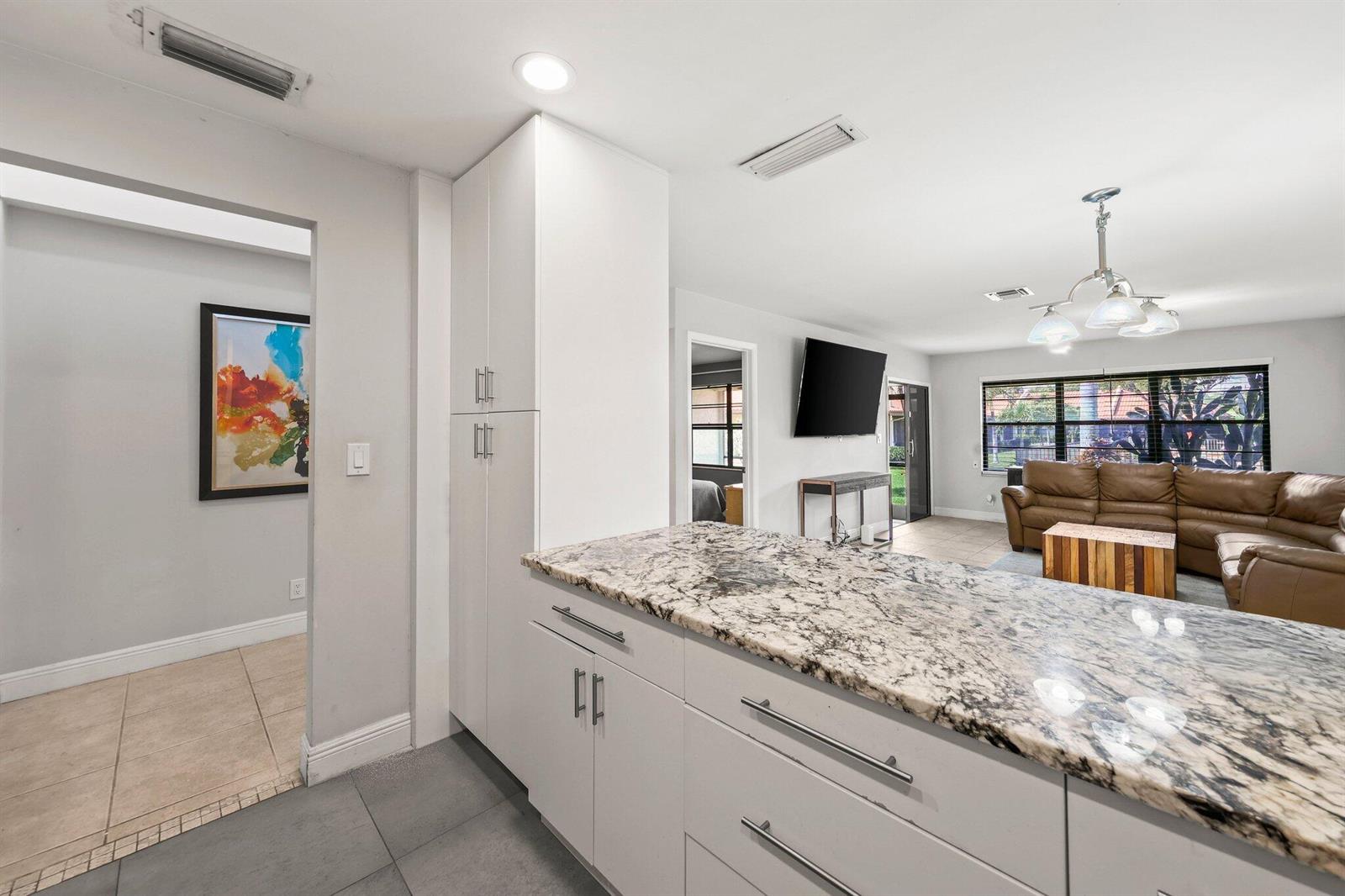 A kitchen island with granite countertops overlooks a living room with a brown leather sofa — 41 Bethesda Park Circle # K41, Boynton Beach FL 33435, BOYNTON BEACH, FL