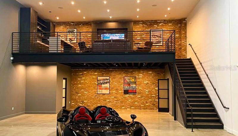 A modern garage features a mezzanine lounge, exposed brick walls, and a black sports car — 11 HARGROVE LANE, PALM COAST, FL