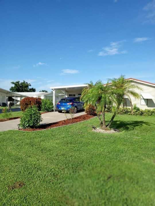 A blue car is parked under a carport next to a single-story house with landscaping — 1640 SW 35th Circle, Okeechobee FL 34974, OKEECHOBEE, FL