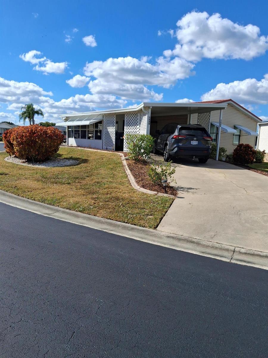 A single-story mobile home features a carport, white lattice accents, and a landscaped front yard — 1640 SW 35th Circle, Okeechobee FL 34974, OKEECHOBEE, FL