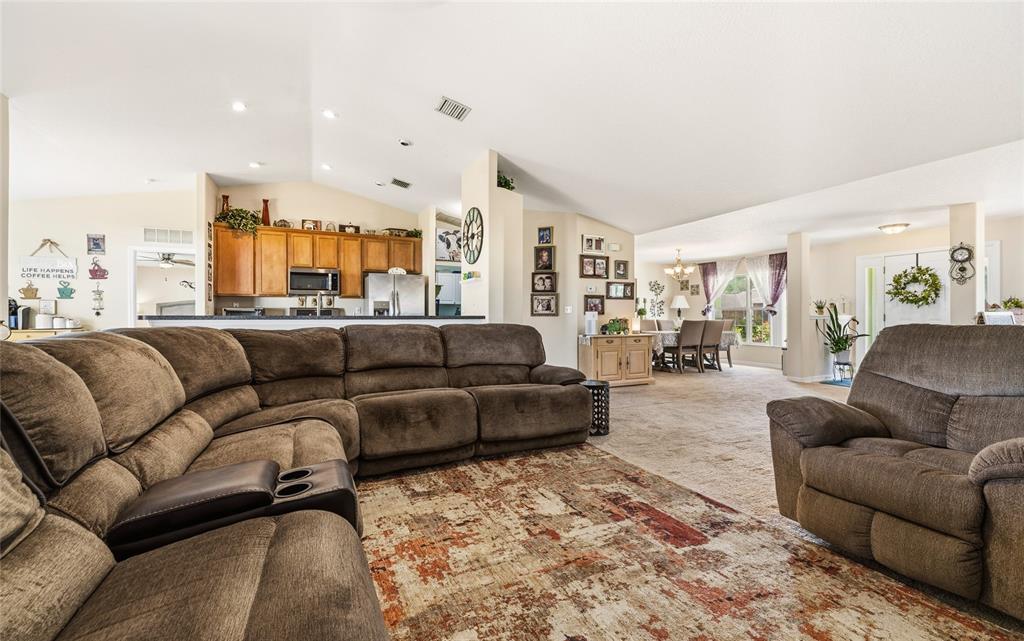 A spacious living room with brown sectional seating, a patterned rug, and an open kitchen — 33 ROYAL LEAF LANE, PALM COAST, FL