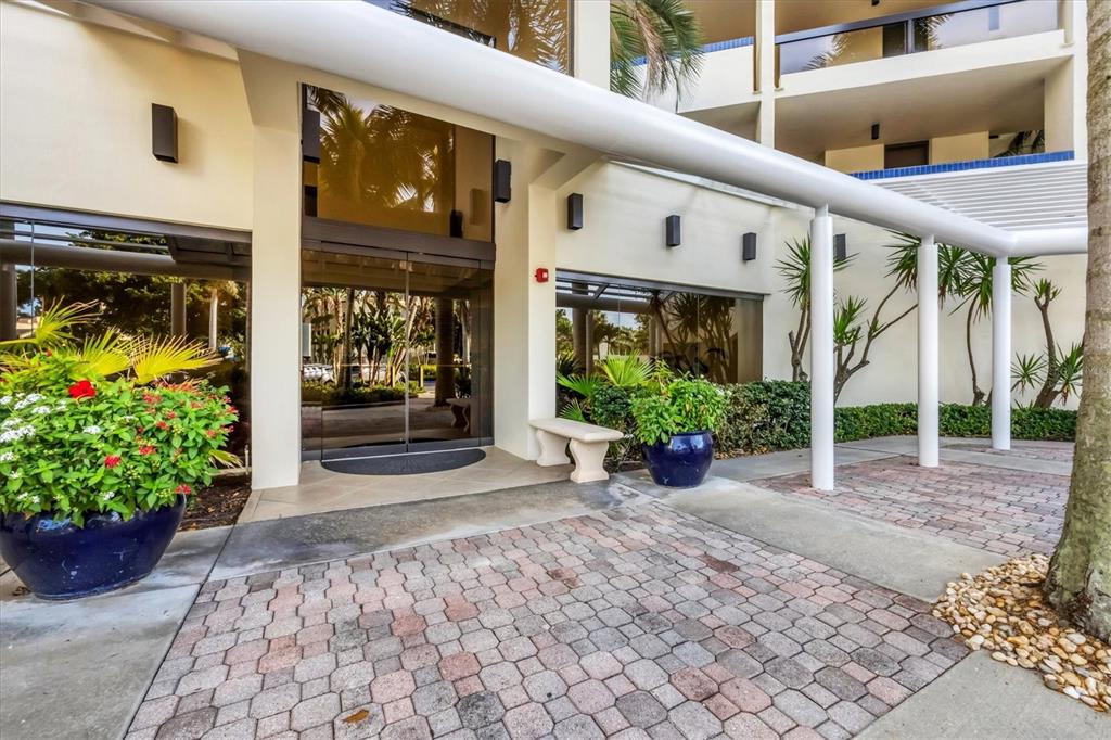 The exterior entrance of a building features a glass door, brick walkway, and potted plants — 1930 HARBOURSIDE DRIVE UNIT 134, LONGBOAT KEY, FL