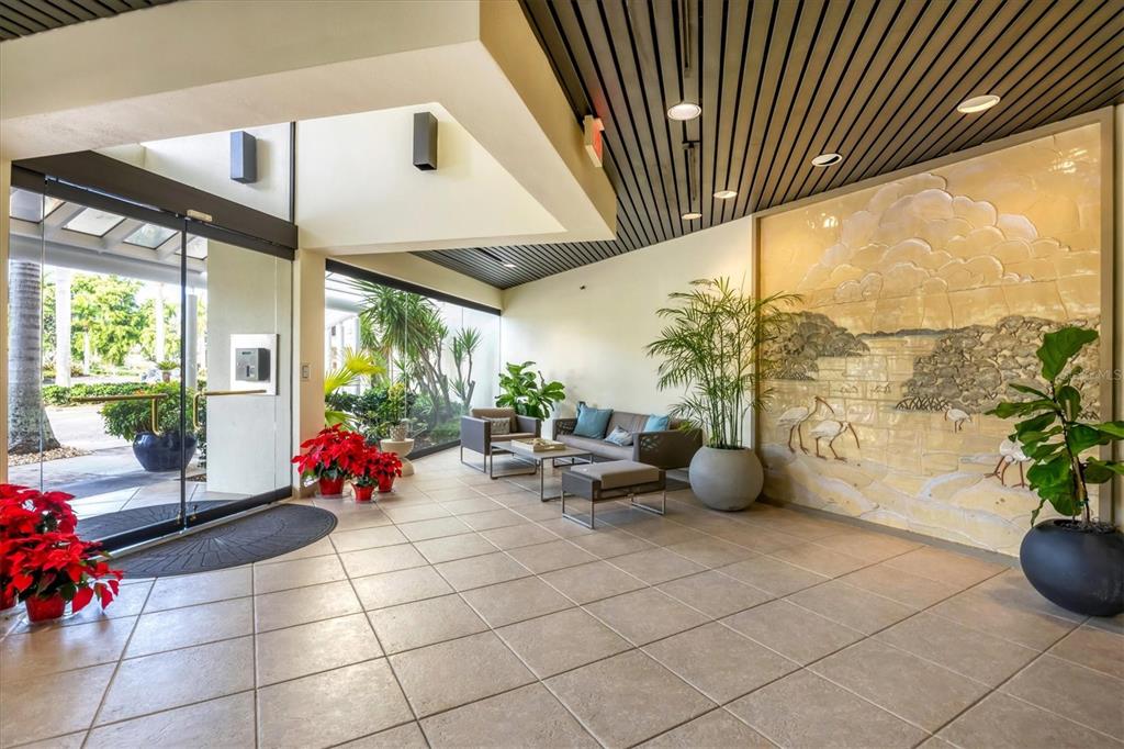 A modern building lobby features tile floors, a textured wall mural, and glass entry doors — 1930 HARBOURSIDE DRIVE UNIT 134, LONGBOAT KEY, FL