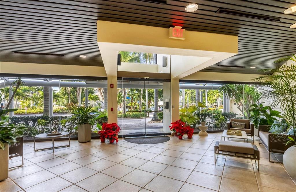 A bright lobby with tile floors, glass walls, and potted poinsettias leads to an outdoor area — 1930 HARBOURSIDE DRIVE UNIT 134, LONGBOAT KEY, FL