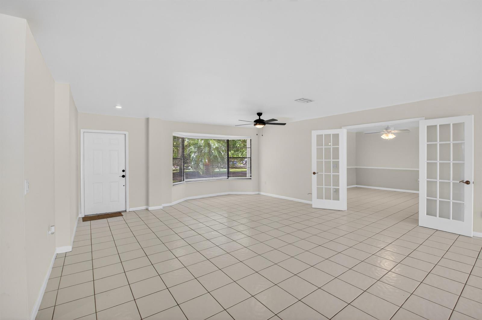 An empty room with beige tile flooring, a bay window, and white French doors — 10157 La Reina Road, Delray Beach FL 33446, DELRAY BEACH, FL