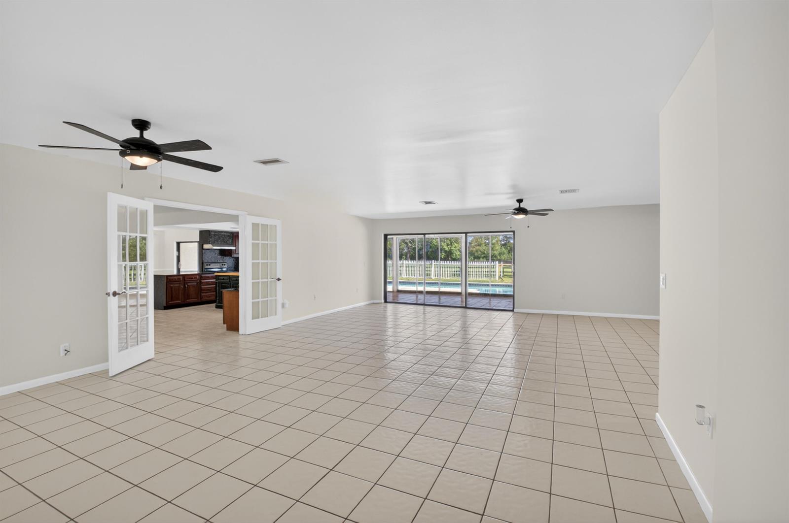 A large, empty room with beige tile flooring, two ceiling fans, and sliding glass doors — 10157 La Reina Road, Delray Beach FL 33446, DELRAY BEACH, FL