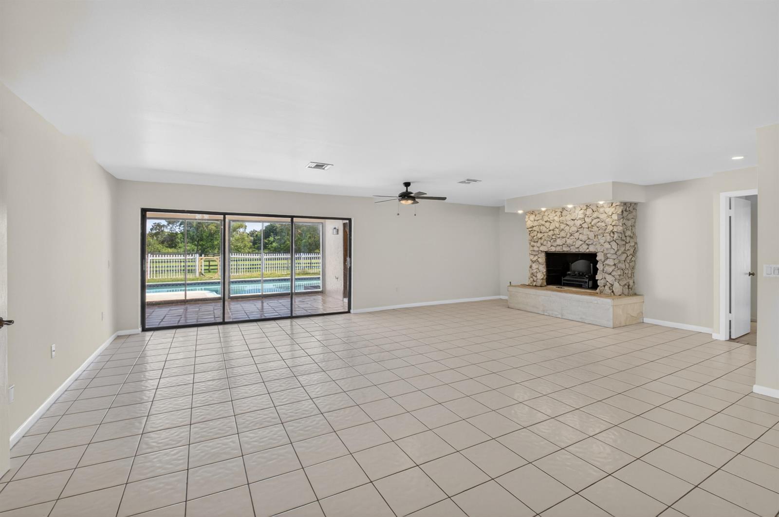 A spacious living room features light tile flooring, a stone fireplace, and sliding glass doors — 10157 La Reina Road, Delray Beach FL 33446, DELRAY BEACH, FL