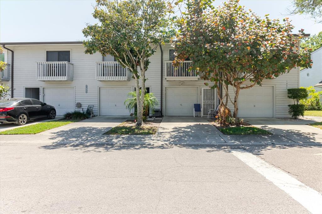 A two-story townhouse exterior features four garage doors, balconies, and mature trees in front — 6420 92ND PLACE UNIT 1202, PINELLAS PARK, FL