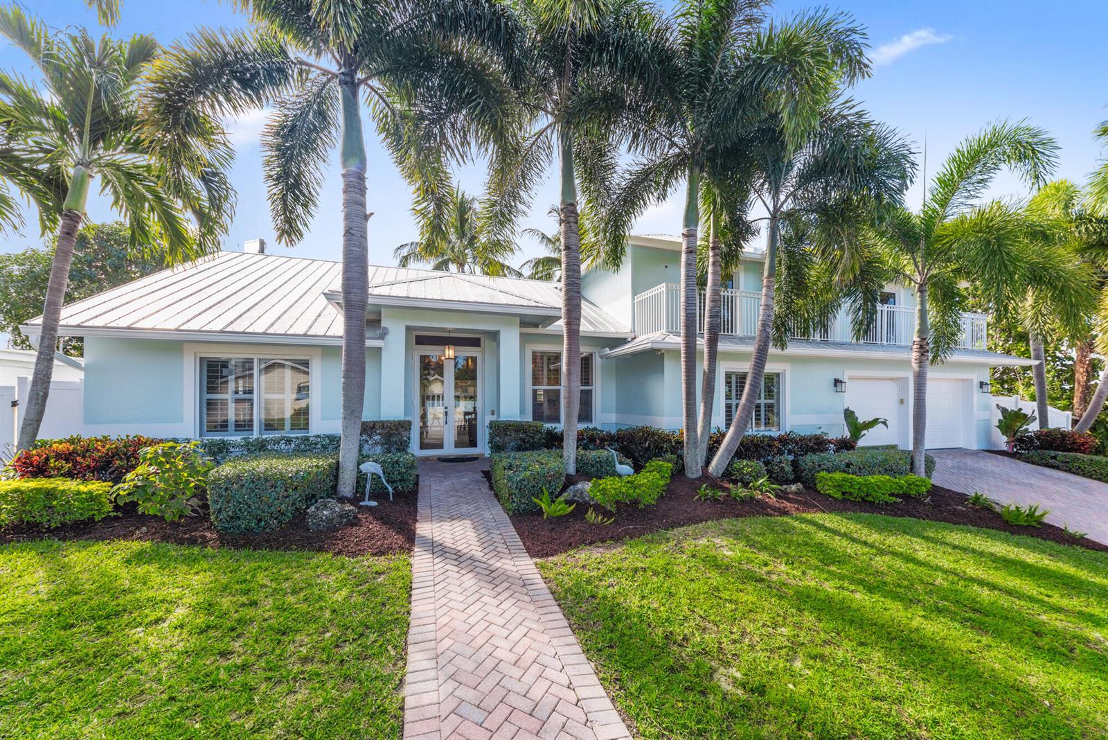 A light blue two-story house with a metal roof, palm trees, and a brick walkway — 490 Mars Way, Juno Beach FL 33408, JUNO BEACH, FL