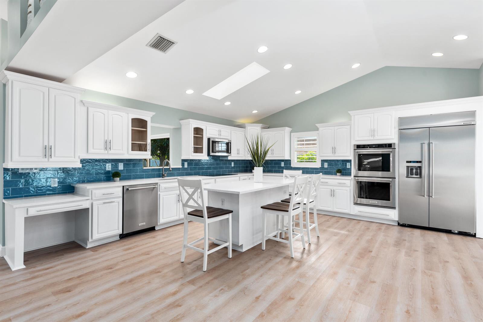 A bright kitchen features white cabinetry, a central island, stainless steel appliances, and blue backsplash — 490 Mars Way, Juno Beach FL 33408, JUNO BEACH, FL