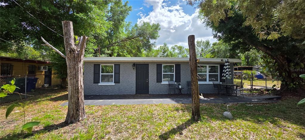 A gray brick exterior house features a black door, shuttered windows, and a patio area — 4215 E HENRY AVENUE, TAMPA, FL