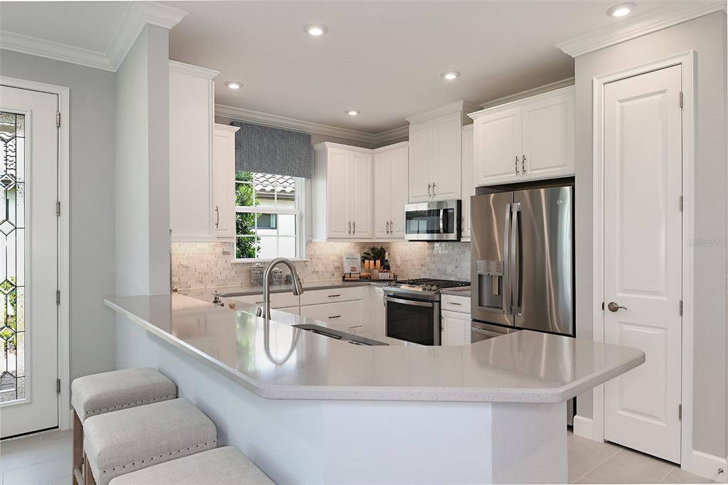 A kitchen features white cabinets, stainless steel appliances, a quartz countertop, and a breakfast bar — 13344 SANTINI CIRCLE, ENGLEWOOD, FL