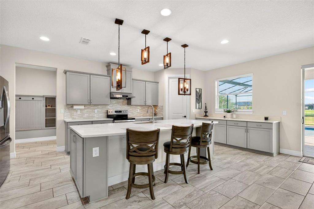 A modern kitchen features gray cabinets, a large white island with barstools, and pendant lighting — 17507 LAGODA LANE, ORLANDO, FL