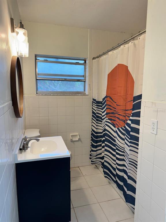 A bathroom features a dark vanity, a round mirror, white wall tiles, and a patterned shower curtain — 517 MOROCCO AVENUE, ORLANDO, FL