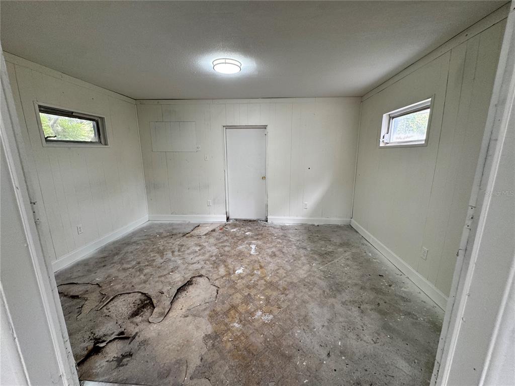 An empty room with white paneled walls, two small windows, and a damaged vinyl floor — 517 MOROCCO AVENUE, ORLANDO, FL