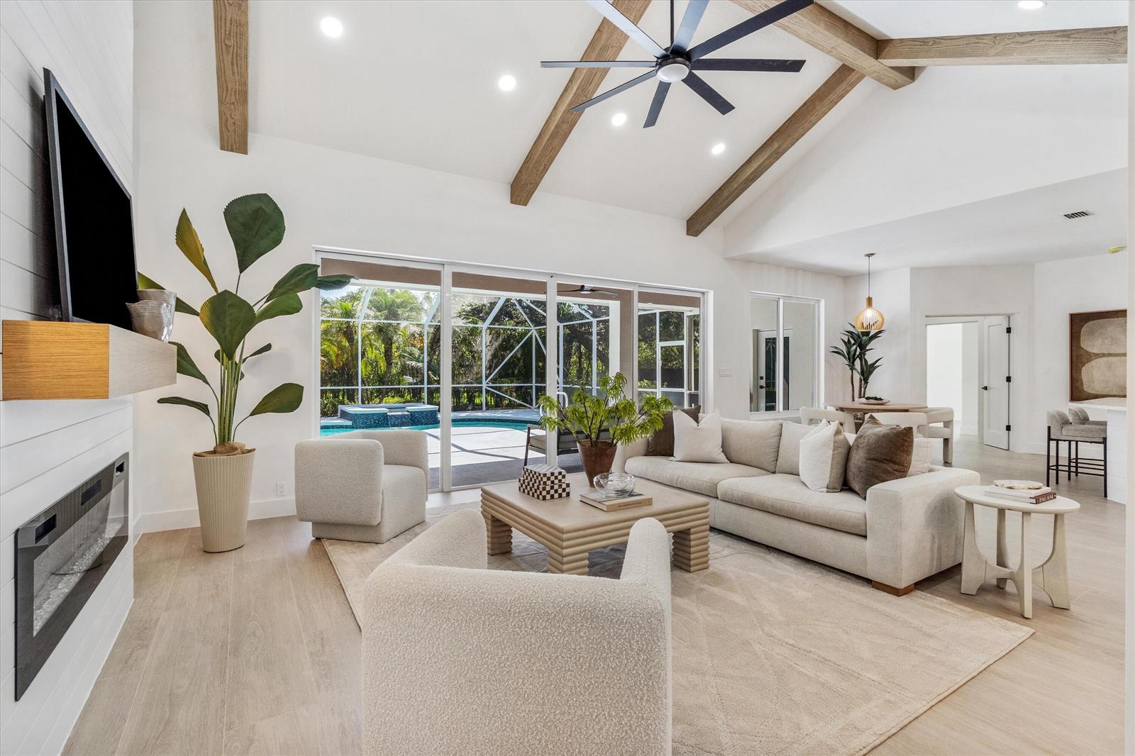 A bright living room features vaulted ceilings with wood beams, a fireplace, and pool views — 19029 SE Kokomo Lane, Jupiter FL 33458, JUPITER, FL