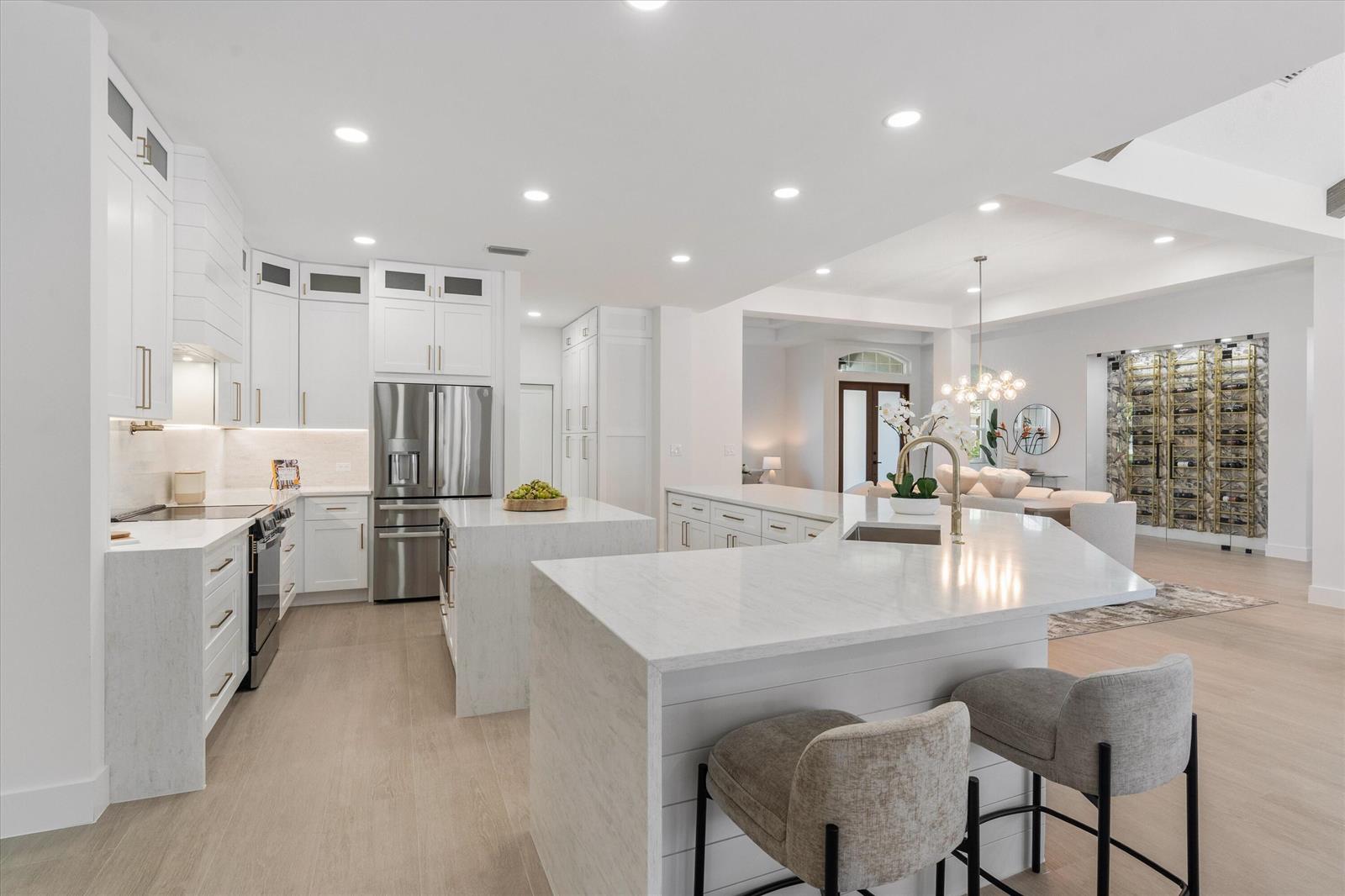 A modern white kitchen features two islands, stainless steel appliances, and light wood flooring — 19029 SE Kokomo Lane, Jupiter FL 33458, JUPITER, FL