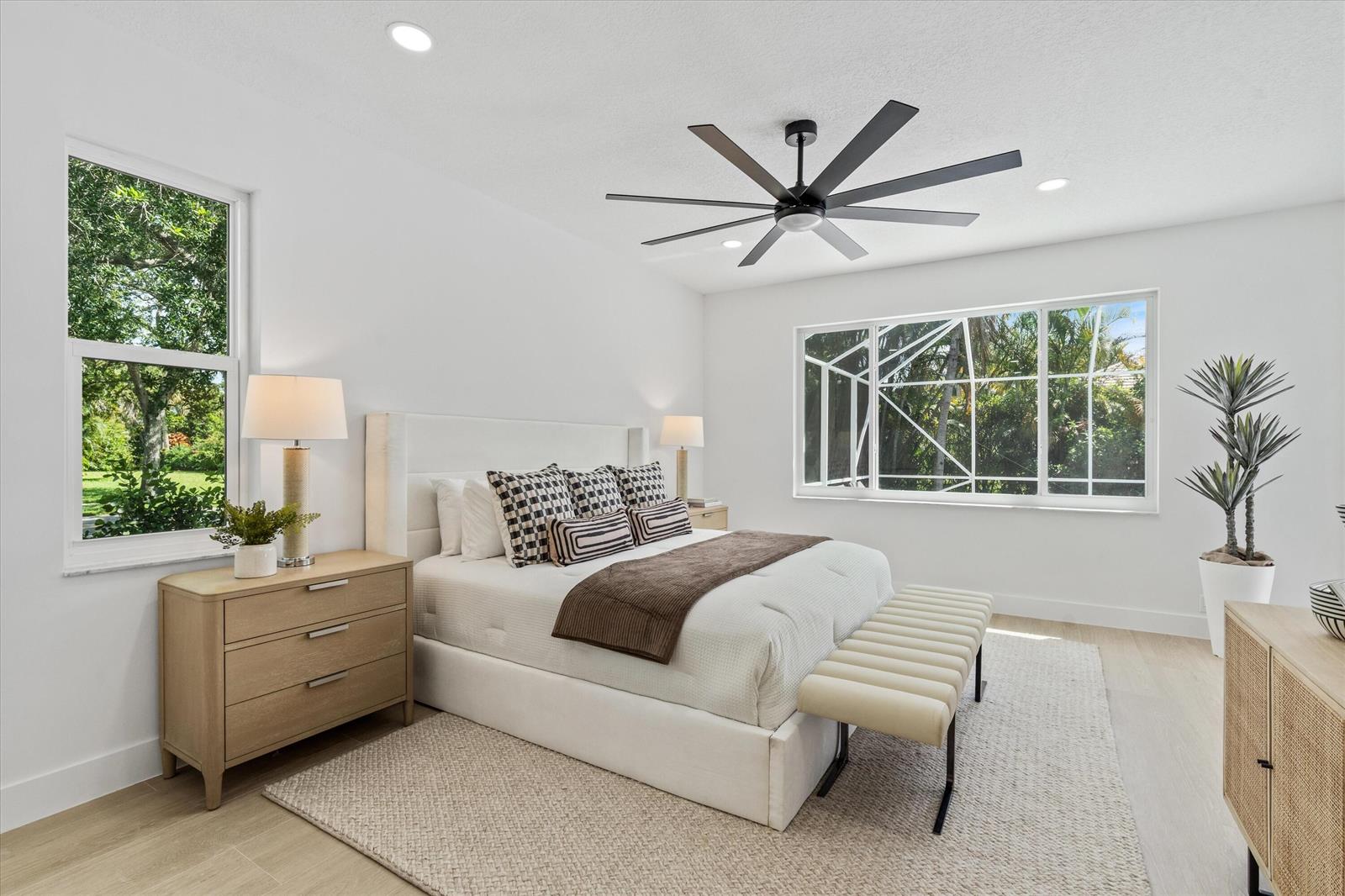 A bright bedroom features a white bed, light wood furniture, and a large ceiling fan — 19029 SE Kokomo Lane, Jupiter FL 33458, JUPITER, FL