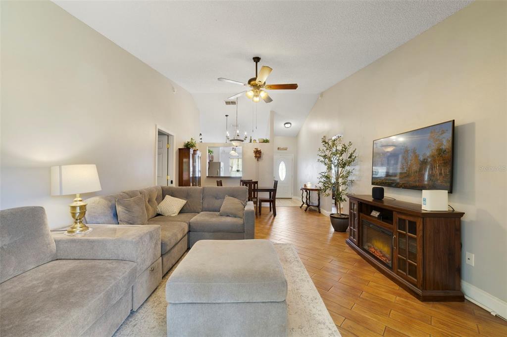 A living room with a grey sectional sofa, wood-look flooring, and a wall-mounted television — 9478 BRACKIN STREET, ORLANDO, FL