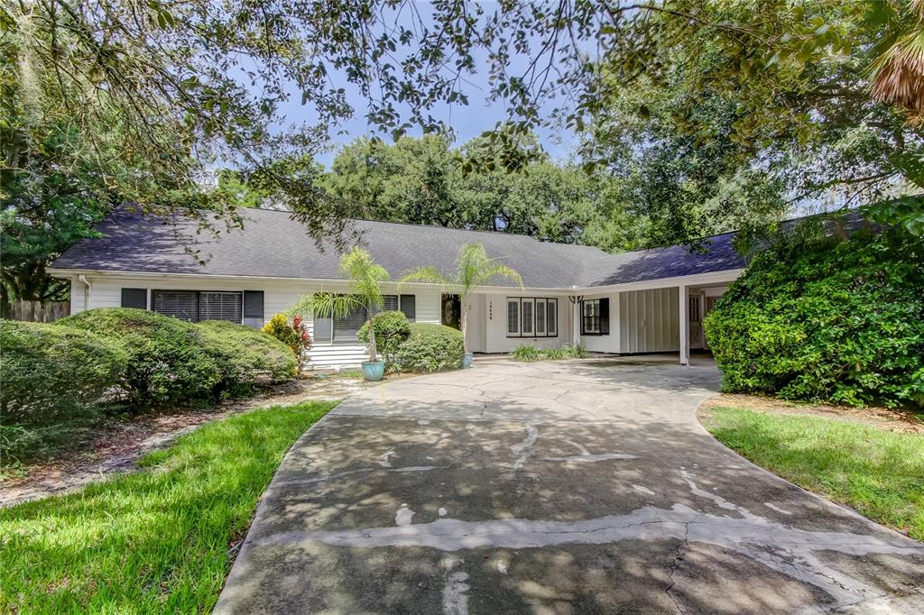 A white single-story house with a dark roof and a large cracked concrete driveway — 10406 RECLINATA LANE, TAMPA, FL