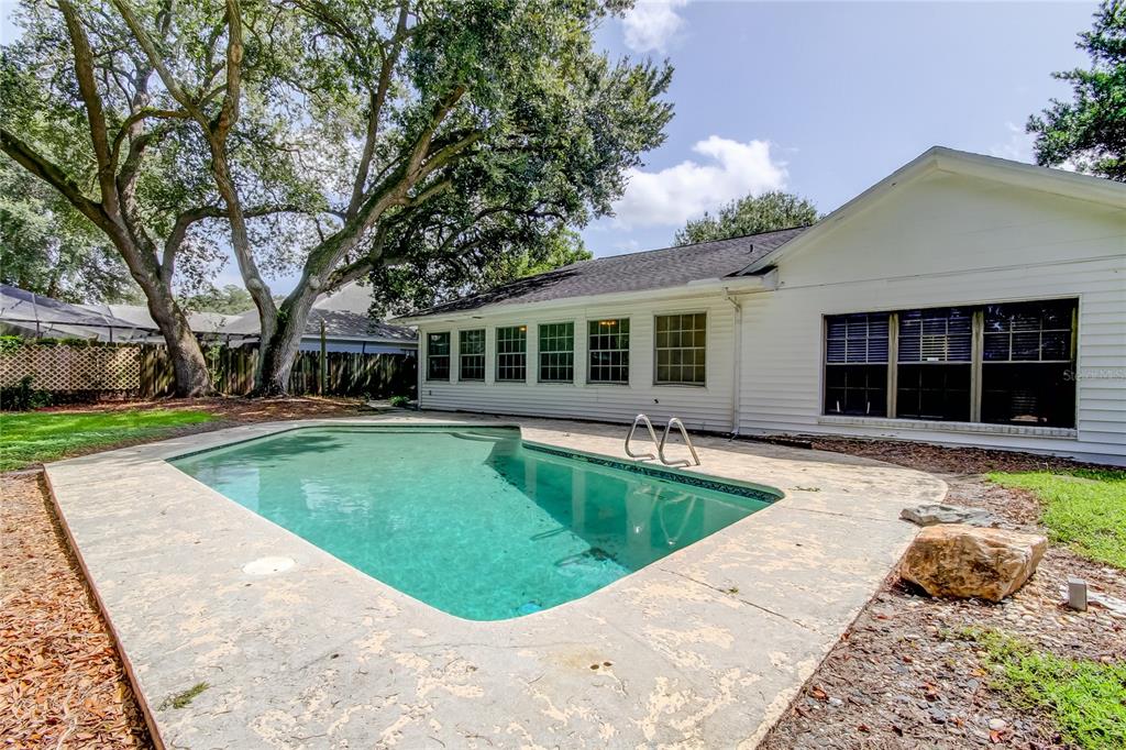 A backyard swimming pool sits on a concrete deck beside a white house with siding — 10406 RECLINATA LANE, TAMPA, FL