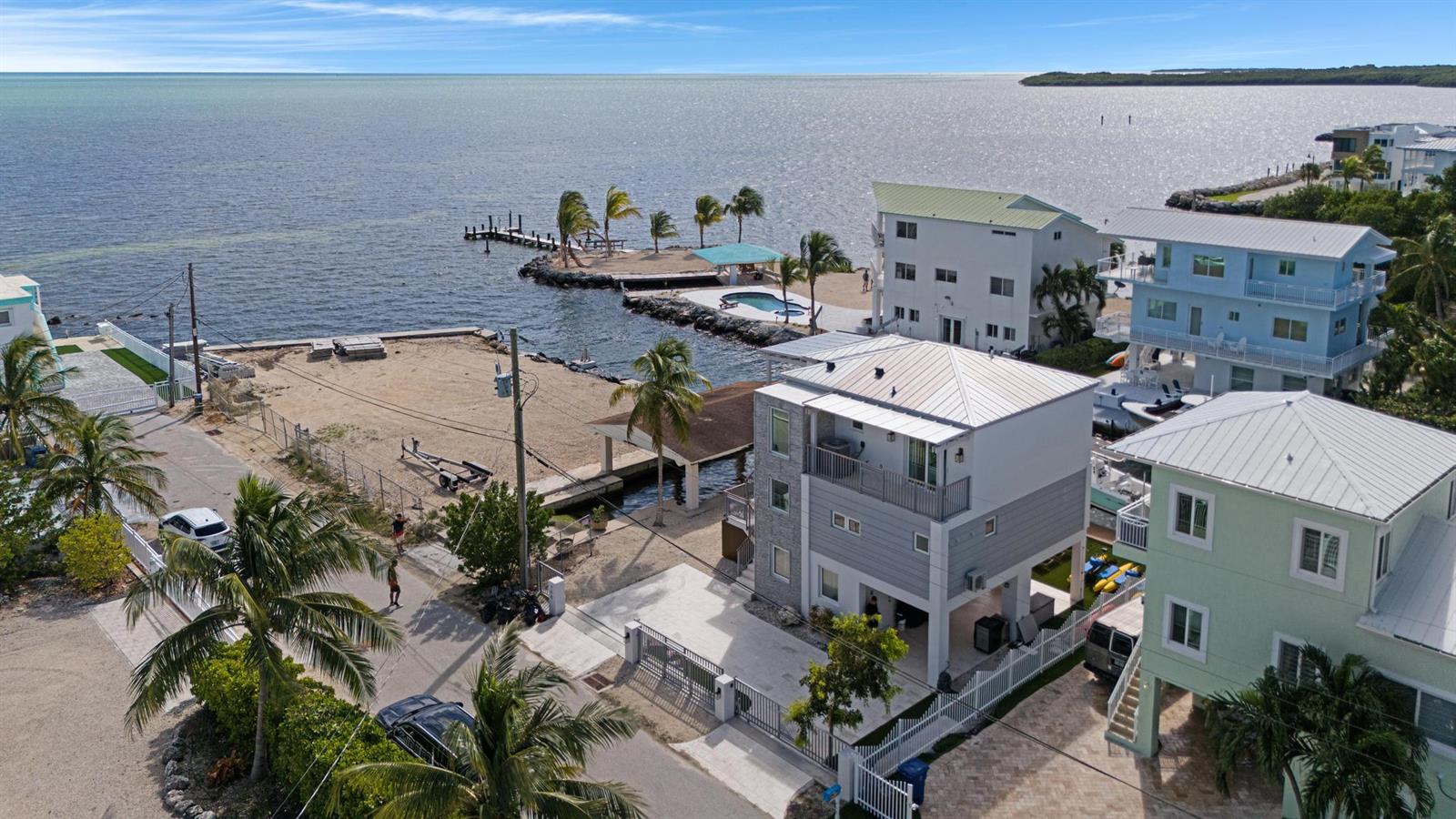 An aerial view shows several multi-story coastal houses near a sandy lot and the ocean — 704 Grouper Lane, Key Largo FL 33037, KEY LARGO, FL