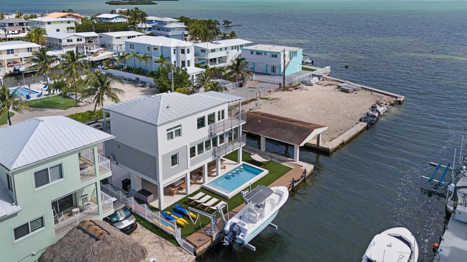 An aerial view shows a multi-story waterfront house with a pool, boat lift, and dock — 704 Grouper Lane, Key Largo FL 33037, KEY LARGO, FL