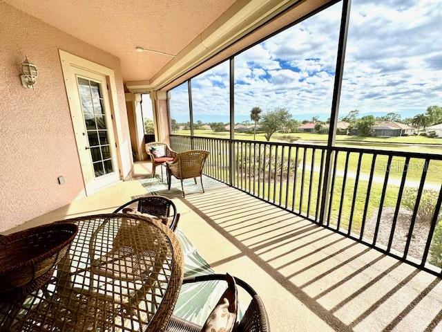 A screened-in balcony features wicker patio furniture and views of a grassy landscape and pond — 24417 BALTIC AVENUE UNIT 1102, PUNTA GORDA, FL