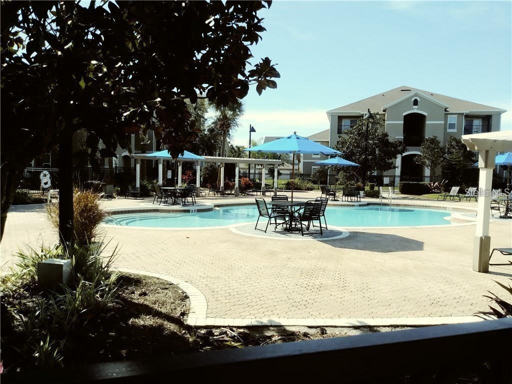 A swimming pool with patio furniture and umbrellas sits in front of a multi-story apartment building — 6512 SWISSCO DRIVE UNIT 1423, ORLANDO, FL